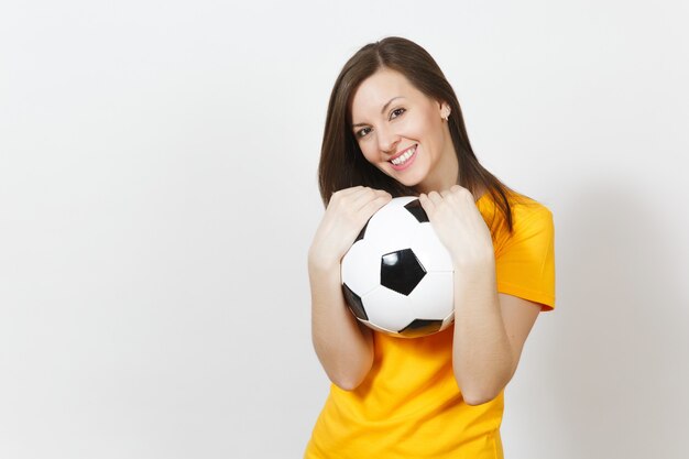 Linda jovem alegre feliz europeia, fã de futebol ou jogador de uniforme amarelo, abraçando uma bola de futebol isolada no fundo branco. Esporte, jogue futebol, saúde, conceito de estilo de vida saudável.