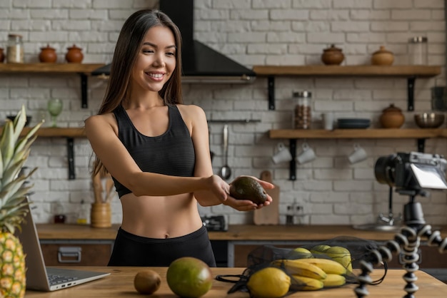 Foto linda jovem asiática blogueira saudável mostrando abacate e comida de dieta limpa