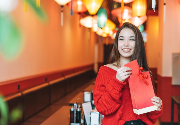 Linda jovem asiática em roupas vermelhas com saco de presentes no restaurante comemorando o Ano Novo Chinês