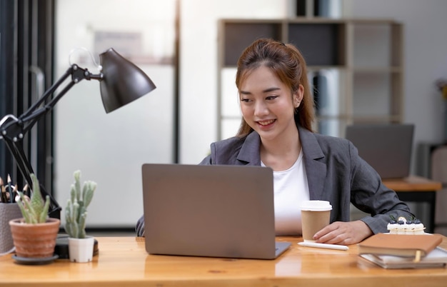 Linda jovem asiática sentada no café usando laptop feliz jovem empresária sentada à mesa no café com o computador superior da guia