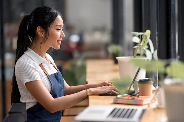 Linda jovem barista asiática no avental usando tablet Verifique a lista de pedidos de bebida do cliente Conceito de inicialização do proprietário da empresa