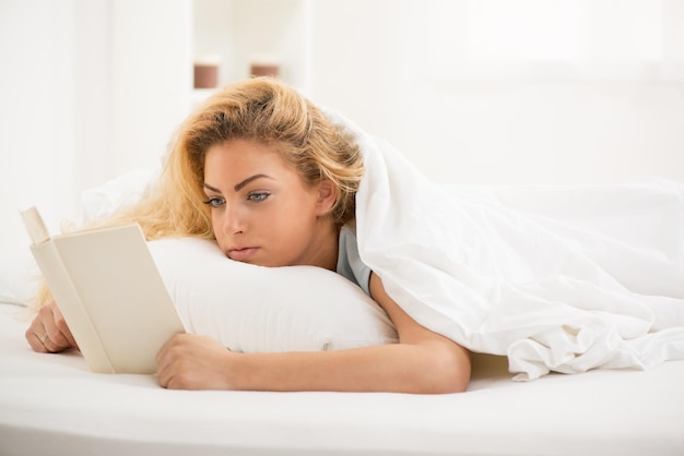 Linda jovem bonita lendo livro na cama