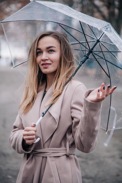 Linda jovem caminha no parque de outono com humor de outono de guarda-chuva transparente brilhante