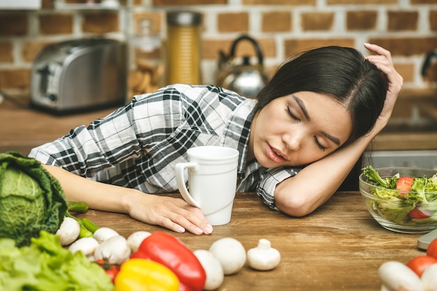 Linda jovem cansada dormindo na mesa da cozinha. Estresse.