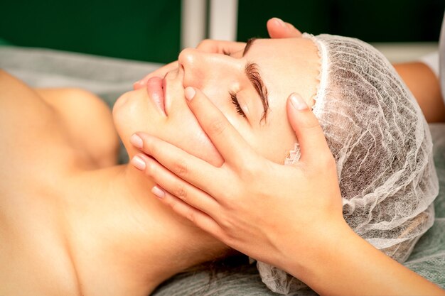 Linda jovem caucasiana com os olhos fechados, recebendo uma massagem facial em um salão de beleza