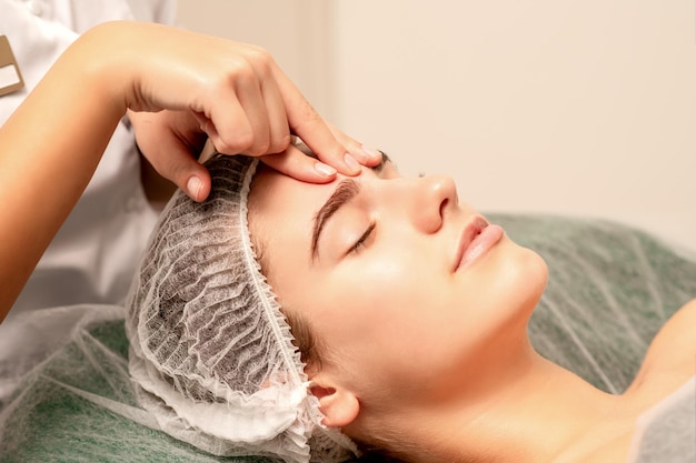 Linda jovem caucasiana recebendo uma massagem facial com os olhos fechados no salão spa close-up Conceito de tratamento relaxante