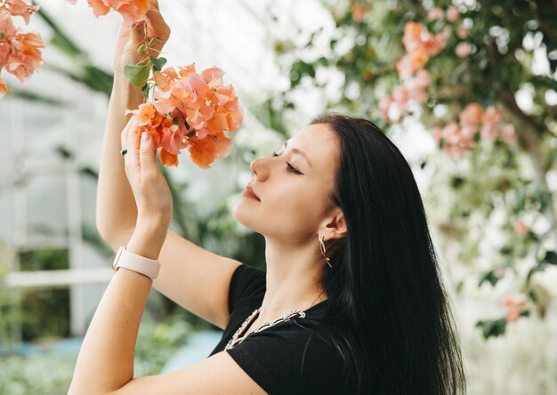 Linda jovem cheirando flores da primavera Lindas flores de buganvílias na mão de uma garota com cabelo escuro esvoaçante