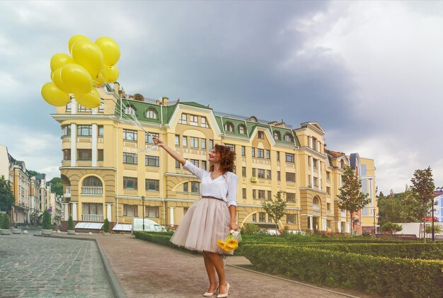 Linda jovem com balões amarelos andando pela cidade