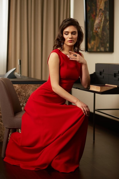 Linda jovem com cabelo castanho em vestido elegante, sentado na cadeira no interior de luxo
