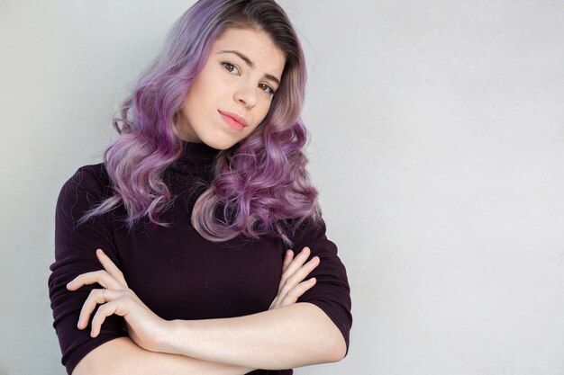 Foto linda jovem com cabelo roxo encaracolado e maquiagem natural se passando perto de uma parede cinza. espaço para texto