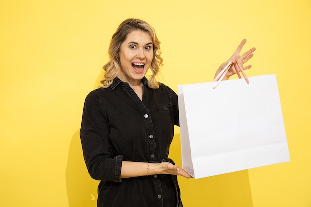 Linda jovem com roupas casuais, feliz com sacolas de presente, compras, férias de primavera, fundo amarelo, estúdio tiro. Comemorando o dia da mulher, aniversário, dia dos namorados, aniversário. Copie o espaço em branco.