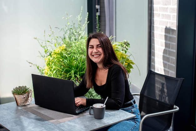 linda jovem com um laptop se senta em uma mesa e trabalha