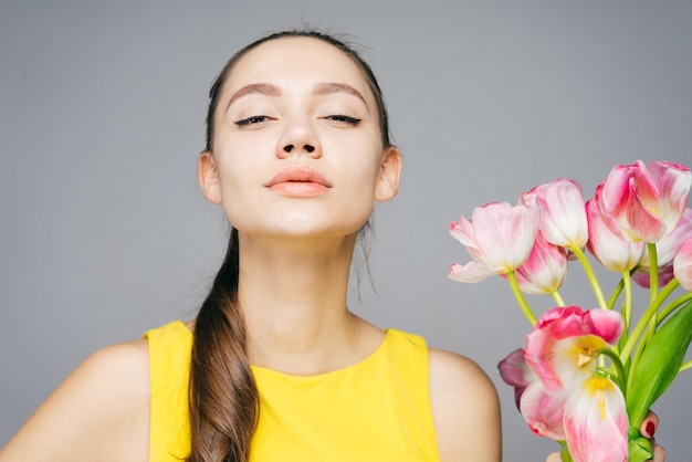 Linda jovem confiante em um vestido amarelo segurando um buquê de flores perfumadas olhando para a câmera