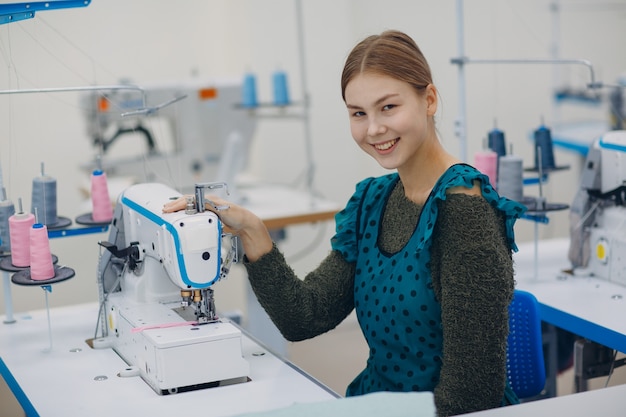 Linda jovem costureira costura na máquina de costura na fábrica.