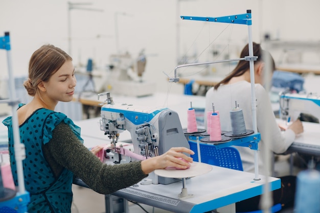 Linda jovem costureira costura na máquina de costura na fábrica.