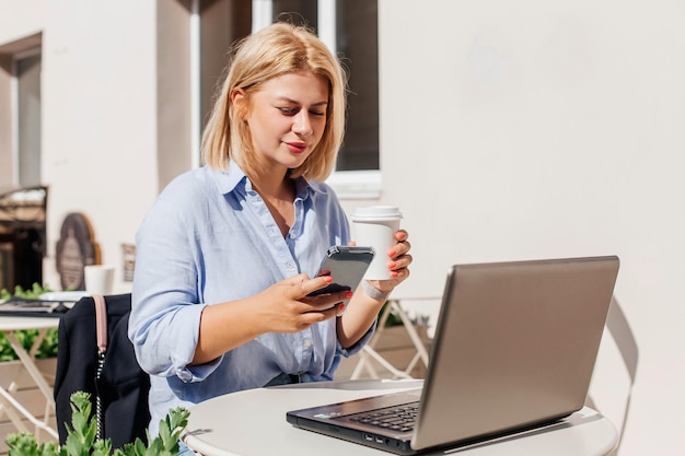 Linda jovem de camisa azul trabalhando em um notebook em um café e bebendo café Trabalho remoto