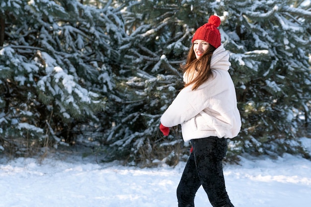 Linda jovem de chapéu vermelho tricotado está caminhando na floresta nevada Retrato em movimento