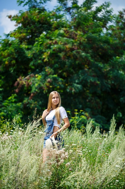 Linda jovem de macacão jeans e um chapéu leve caminhando no parque