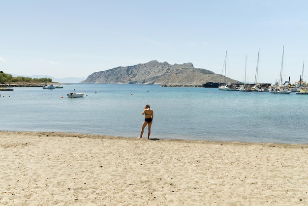 Linda jovem de maiô aproveita as férias de verão na praia com iates ao fundo perto