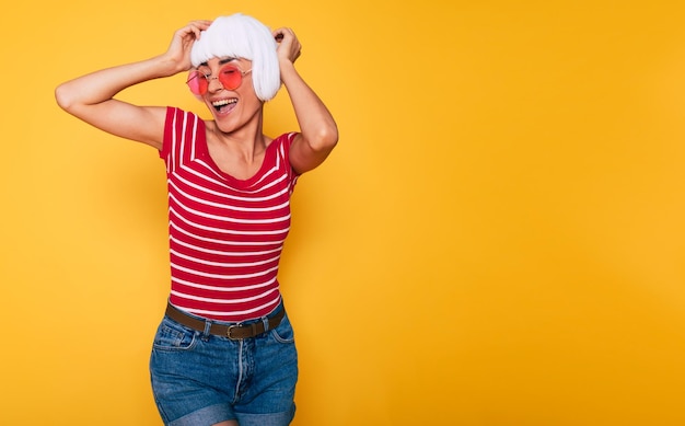 Linda jovem de peruca loira e óculos de sol rosa se divertindo em fundo laranja moda loira posando