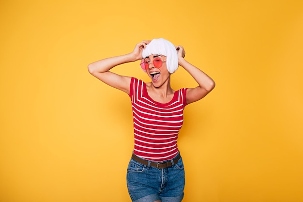 Linda jovem de peruca loira e óculos de sol rosa se divertindo em fundo laranja moda loira posando