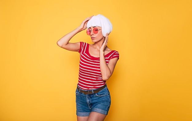 Linda jovem de peruca loira e óculos de sol rosa se divertindo em fundo laranja moda loira posando