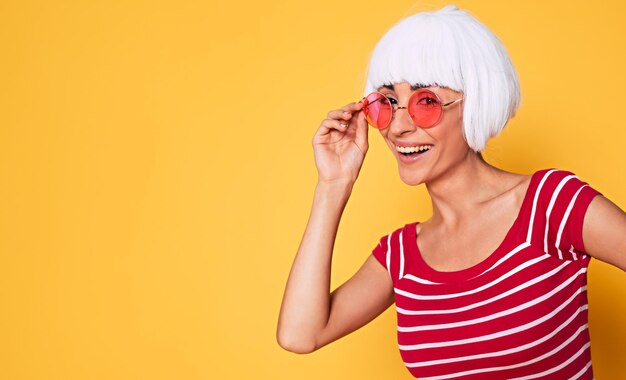 Linda jovem de peruca loira e óculos de sol rosa se divertindo em fundo laranja moda loira posando