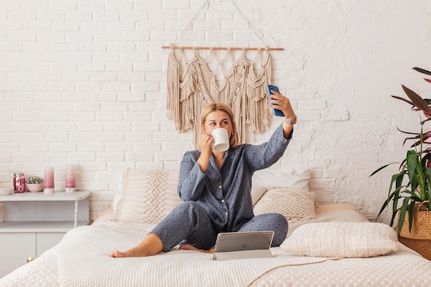 Foto linda jovem de pijama trabalhando em um laptop na cama falando ao telefone compras on-line