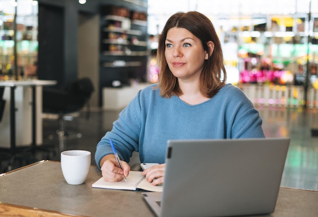 Linda jovem elegante com corpo de tamanho positivo usando laptop no escritório do salão de beleza