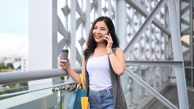 Linda jovem elegante com sacolas de compras falando no celular em pé no terraço do shopping