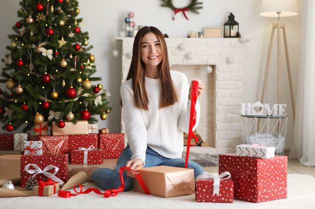 Linda jovem embalando presentes de Natal em um interior de casa decorado