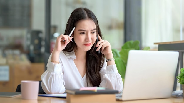 Linda jovem empresária asiática encantadora falando ao telefone celular no escritório.