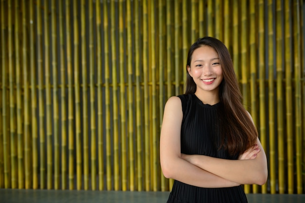 Linda jovem empresária asiática feliz sorrindo com os braços cruzados contra a cerca de bambu