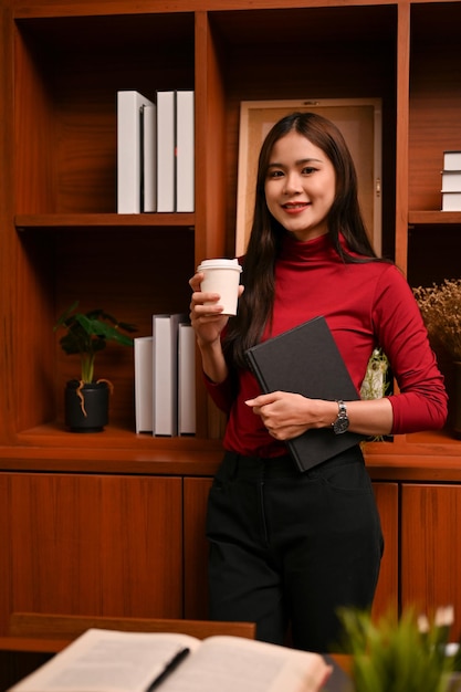 Linda jovem empresária asiática no escritório com sua xícara de café e livro