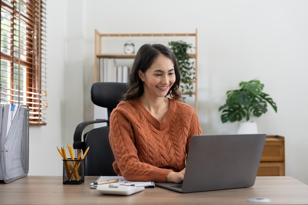 Linda jovem empresária asiática sorridente trabalhando em laptop e bebendo café Empresária asiática trabalhando em finanças e calculadora em seu escritório