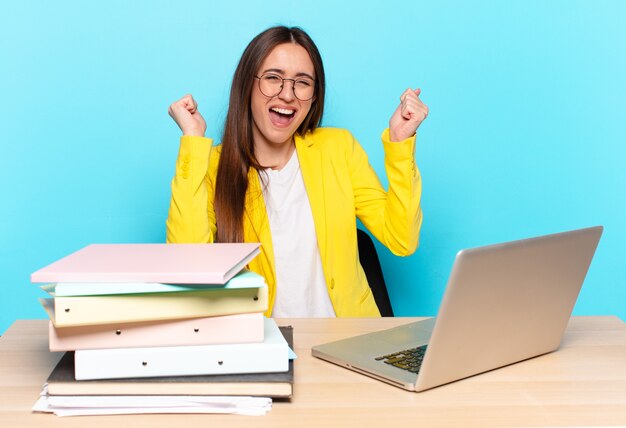 Linda jovem empresária parecendo extremamente feliz e surpresa, comemorando o sucesso, gritando e pulando