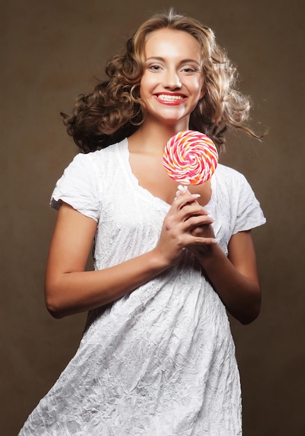 Linda jovem encaracolada segurando um pirulito branco vermelho e sorrindo