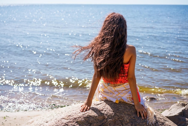 Linda jovem esbelta com cabelo comprido ondulado senta-se à beira-mar em grande