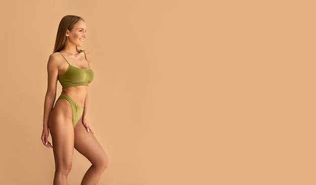 Linda jovem esportiva bronzeada em roupas íntimas esportivas verdes em um fundo bege