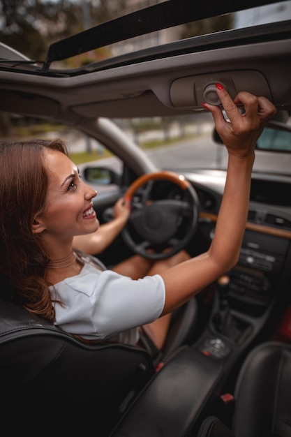 Foto linda jovem está abrindo a janela do telhado enquanto dirige um carro.