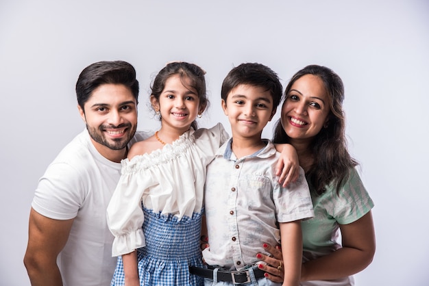 Linda jovem família indiana de quatro pessoas se abraçando, olhando para a câmera e sorrindo em pé contra um fundo branco