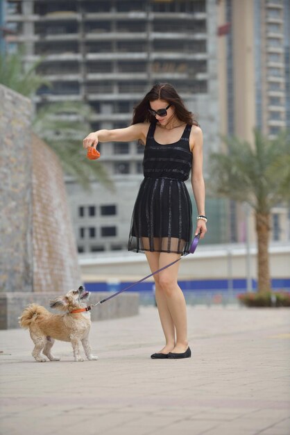 Linda jovem feliz de vestido preto com cachorrinho fofo se divertir na rua