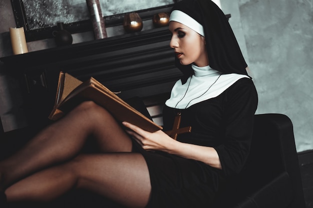 Foto linda jovem freira em terno preto religião contém bíblia e posando para a câmera com um grande livro sobre um fundo preto. fechar-se. conceito de religião.