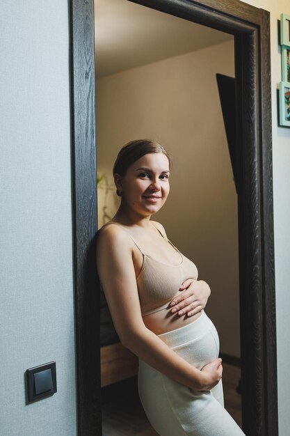 Linda jovem grávida com roupas de maternidade casuais e bonitas Linda grávida abraçando a barriga em casa