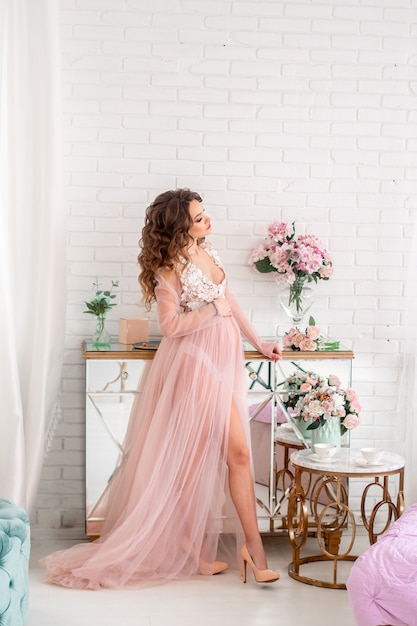 Linda jovem grávida com um vestido rosa em casa