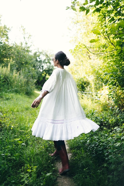 Linda jovem indiana cheirando flores no parque usando vestido branco