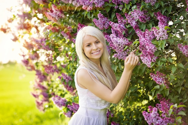 Linda jovem loira sorridente de vestido branco com flores lilás