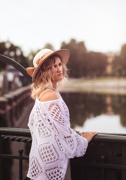 Linda jovem loira usando vestido e chapéu de palha aproveitando o nascer do sol à beira-mar na velha cidade europeia Moda e estilo Viagens de verão