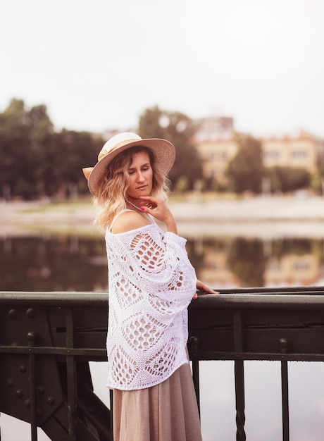 Linda jovem loira usando vestido e chapéu de palha aproveitando o nascer do sol à beira-mar na velha cidade europeia Moda e estilo Viagens de verão