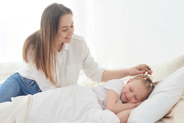 Linda jovem mãe acorda sua filha pré-adolescente pela manhã. Ternura e cuidado. Amor de mãe.